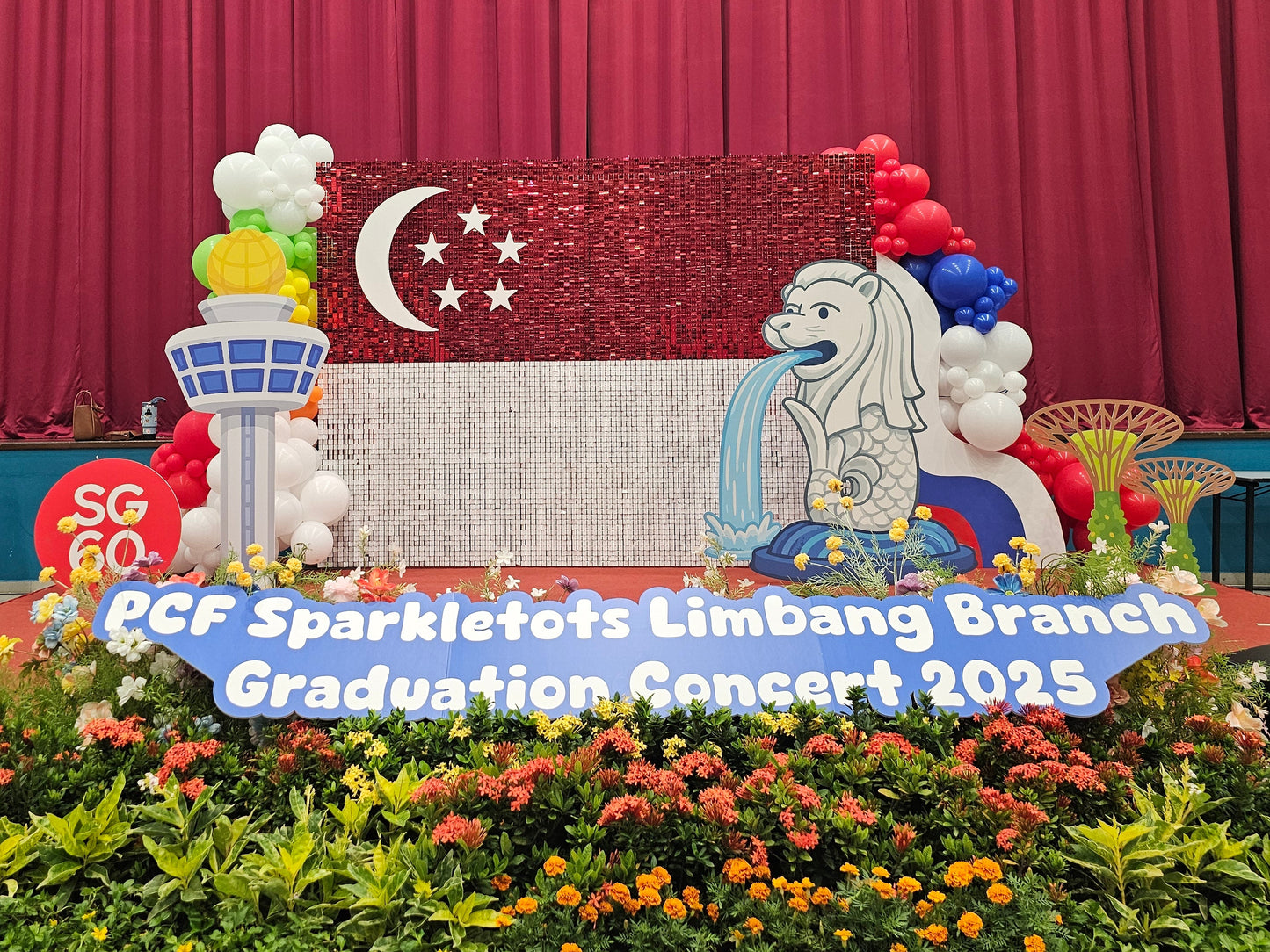 Decorated stage with Singapore flag and floral arrangements for PCF Sparkletots Limbang Branch Graduation Concert 2025.